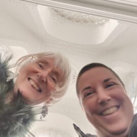Claudia Canella and Davina Kirkpatrick smiling showing Modern Museum of art stairwell above them.