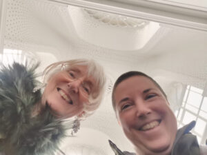 Claudia Canella and Davina Kirkpatrick smiling showing Modern Museum of art stairwell above them.