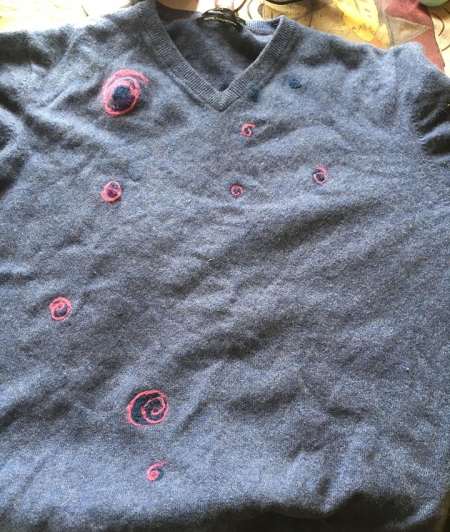 a blue-grey cashmere jumper with visible pink and dark blue needle-felted mending swirls.